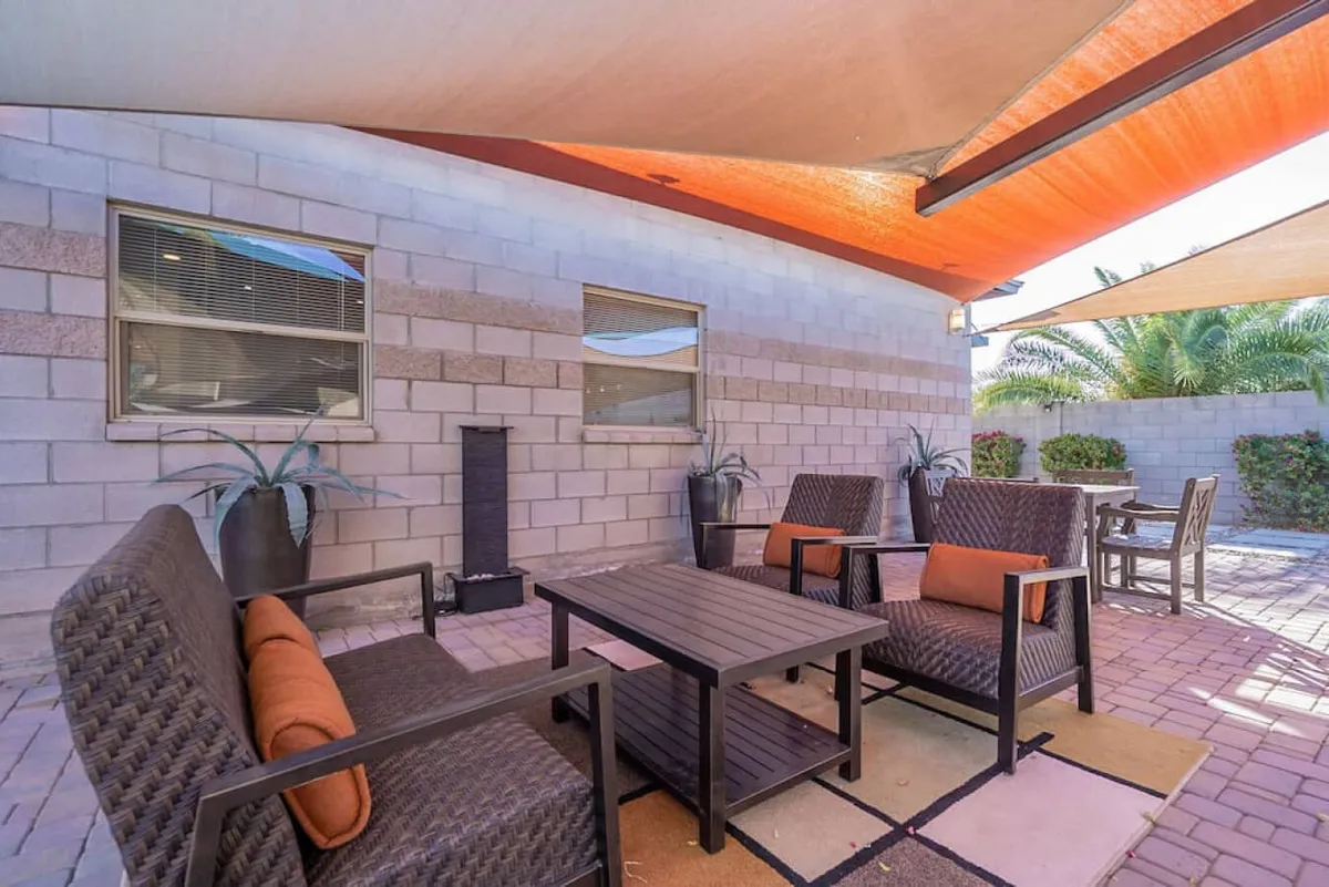 This image shows an inviting exterior seating area surrounded by decorative plants and shaded by attractive sails. The arrangement of comfortable seating encourages social gatherings, dining, or simply enjoying the peaceful neighborhood ambiance.