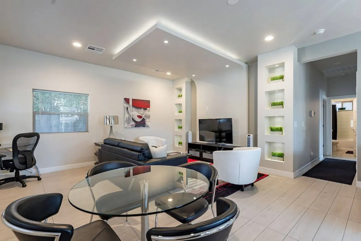 A contemporary, open-plan living area showcasing a black leather sofa, glass dining table, wall-mounted TV, and tasteful artwork. Natural light pours in, highlighting the relaxed and airy atmosphere perfect for socializing or unwinding after a day of exploring.
