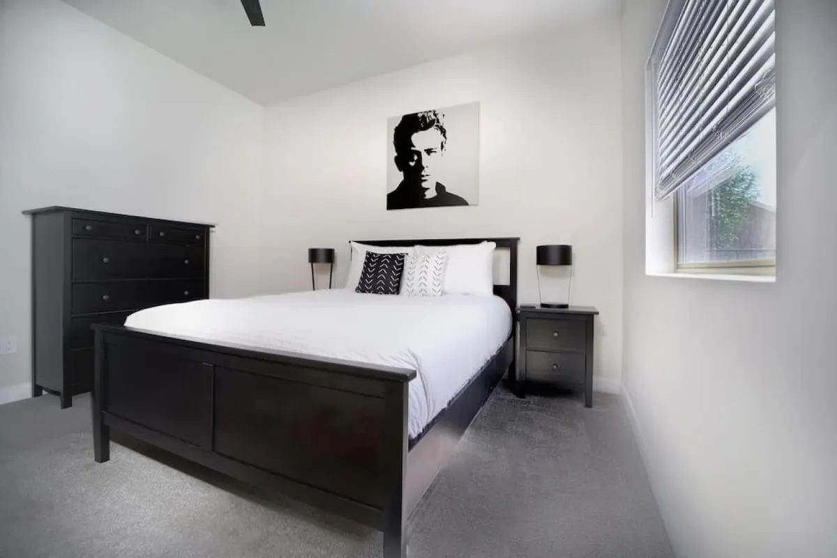 A serene bedroom featuring a plush bed with decorative pillows, black and white artwork above the headboard, and nightstands with ambient lamps. Natural light gently filters through a window, creating a peaceful and restorative atmosphere.