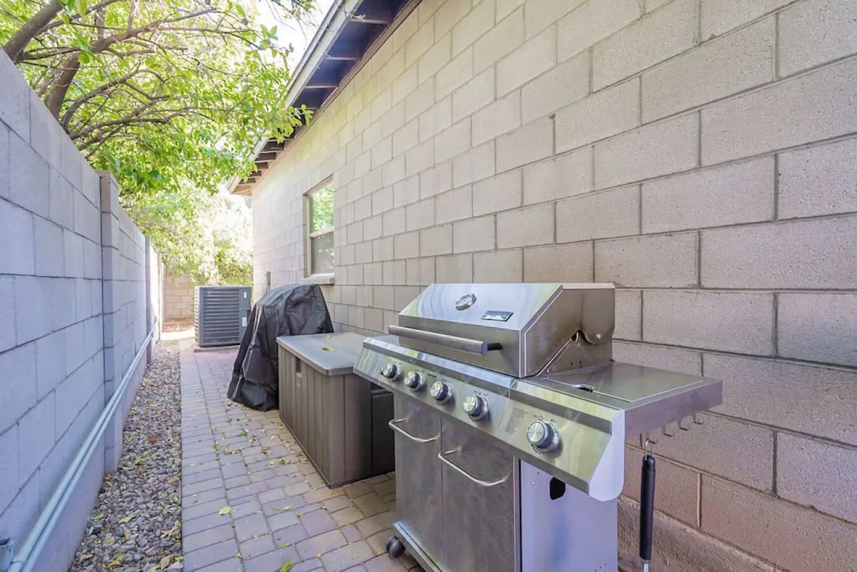 A relaxed courtyard view featuring a grill and an outdoor counter, set along a landscaped pathway. The setup suggests a space designed for barbecuing, casual dining, and social interaction. The scene is open yet intimate, emphasizing easy accessibility and communal enjoyment.