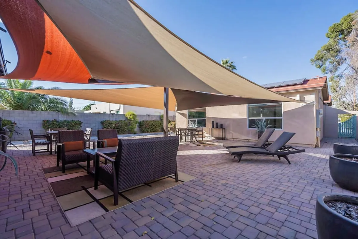 This image showcases a welcoming outdoor seating area set beneath shade sails, with a sparkling swimming pool as the backdrop. Comfortable lounge chairs and a dining area suggest a communal yet private space for both relaxation and casual gatherings.