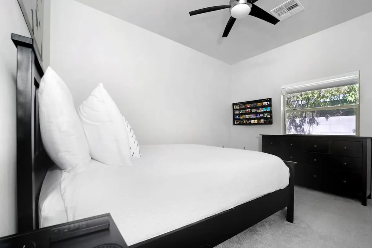 A cozy bedroom with a bed dressed in soft pillows, a dresser for ample storage, a wall-mounted display of personal photos, and a sunlit window. The room exudes warmth and offers a restful space for unwinding.