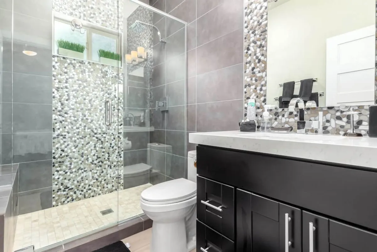 A modern bathroom featuring a glass shower enclosure with mosaic tile accents, a sleek dark vanity, and a well-lit mirror. The atmosphere feels spa-like and inviting, perfect for self-care and rejuvenation.