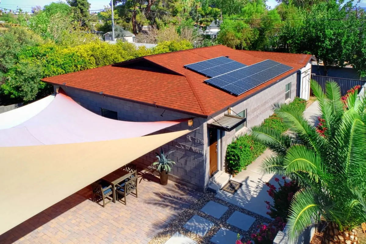 This image features a shaded outdoor dining area beneath a canopy, with a lush green backdrop and prominent solar panels on the roof. The scene conveys a relaxed, eco-friendly atmosphere, ideal for group gatherings or quiet moments. The greenery and canopy provide a sense of privacy and comfort, while the dining setup hints at shared meals and outdoor enjoyment.