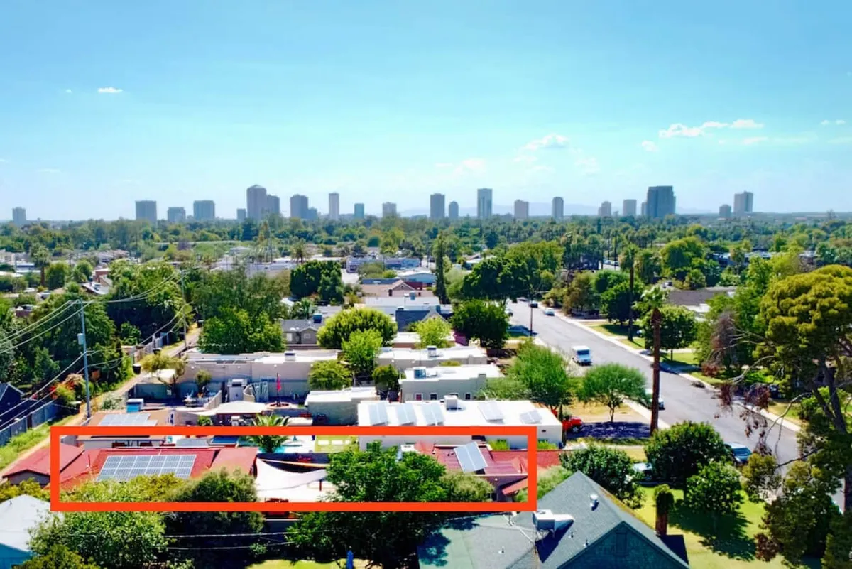 A panoramic rooftop view featuring solar panels, lush green trees, and the Phoenix city skyline in the distance. The image also subtly hints at community activity and outdoor relaxation, with a bright, optimistic feel.
